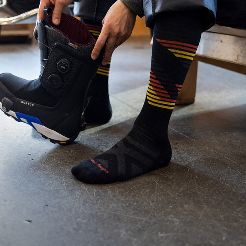 A snowboarder wearing the Men's Carve socks in black with pops of orange and yellow stripes