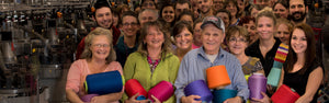 A whole smiling group of Darn Tough employees at the Mill holding Merino Wool yarn