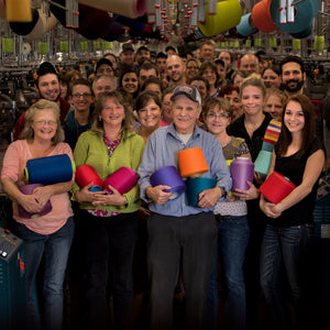 A smiling group of Darn Tough employees at the Mill holding Merino Wool yarn