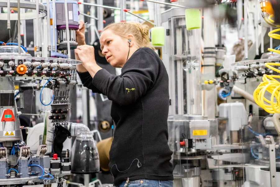 Woman at Darn Tough Mill working to fix a knitting machine