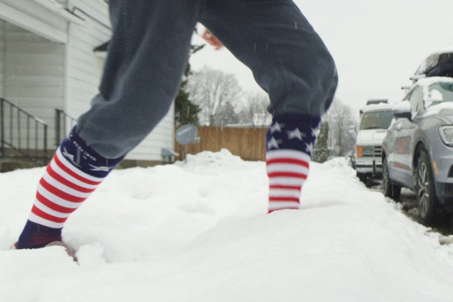 Man walking through snow wearing Captain Stripe over the calf ski socks
