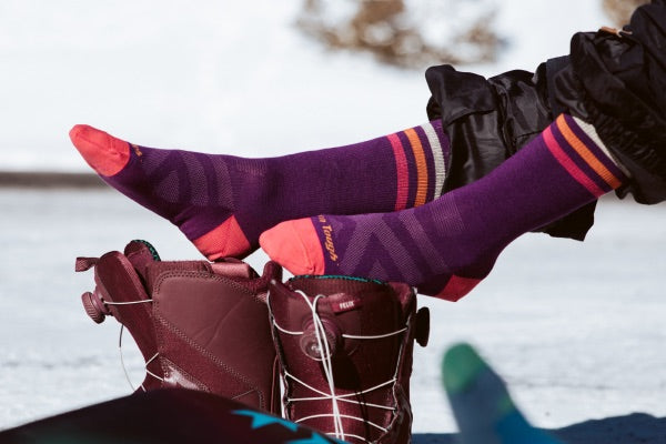 Snowboarder pulling on purple wool lightweight snowboard socks