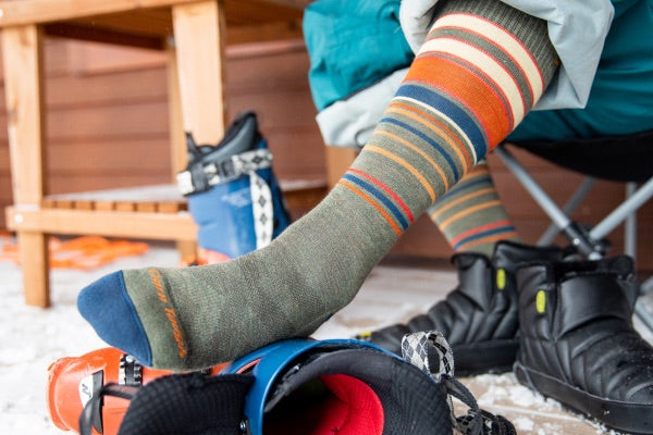 Skier resting socked feet on their boots, wearing striped midweight socks for skiing, warm ski socks all season long