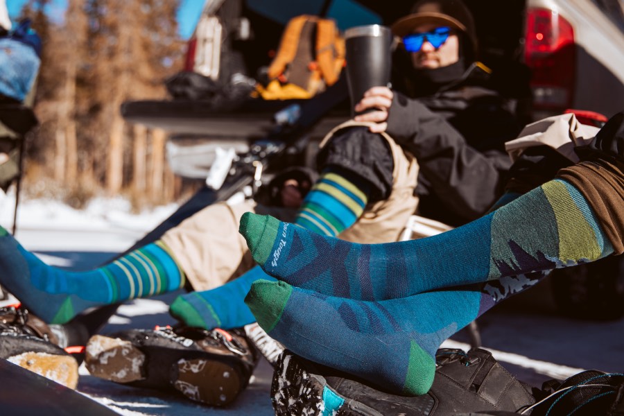 Two sets of sock-clad feet in wool ski socks taking it easy after a fun day on the mountain