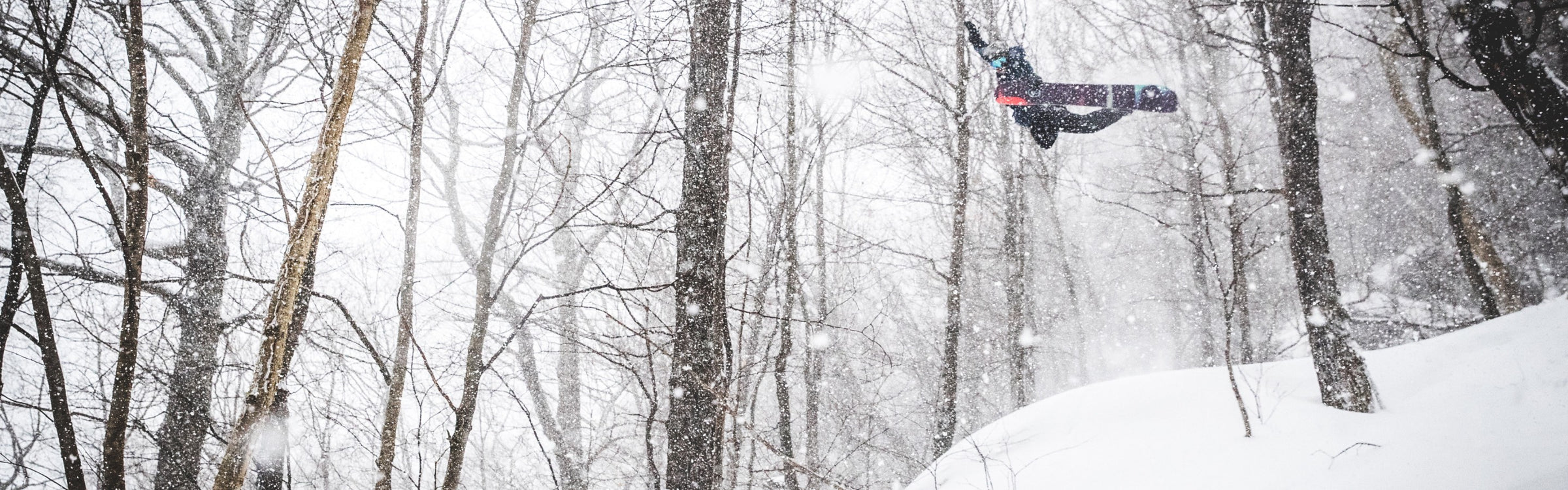 Snowboarder Jake Blauvelt getting some air while winter snow falls around him, wearing wool snowboard socks