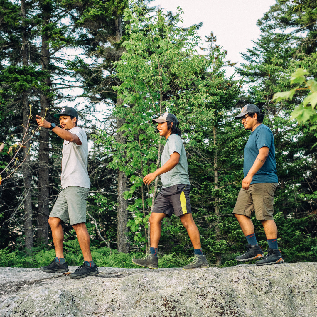 Side shot of 3 models walking across a rock path in the woods all wearing darn tough hiking socks