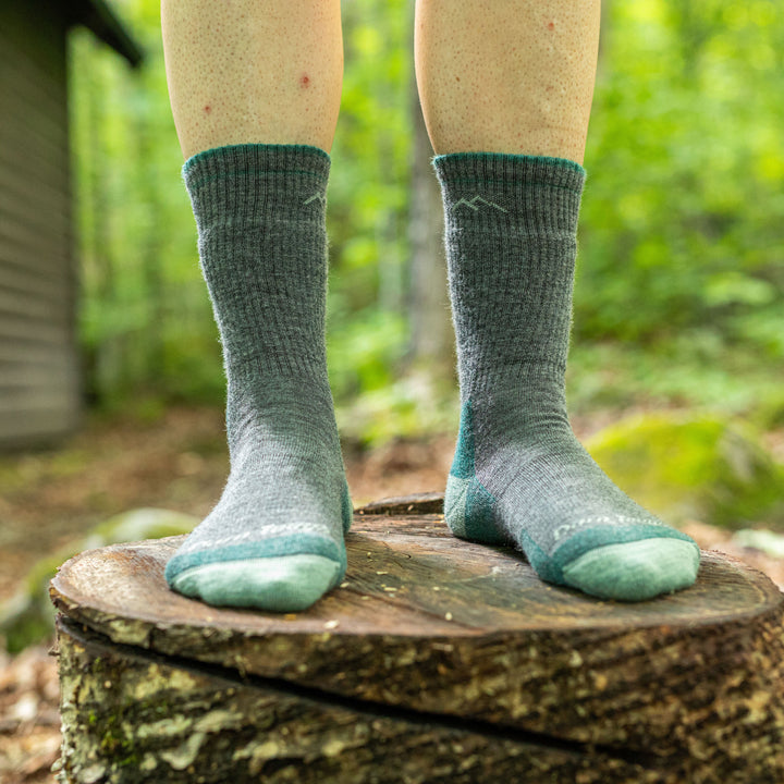 Close up lifestyle shot of model standing on stump wearing hiker boot socks in Slate.