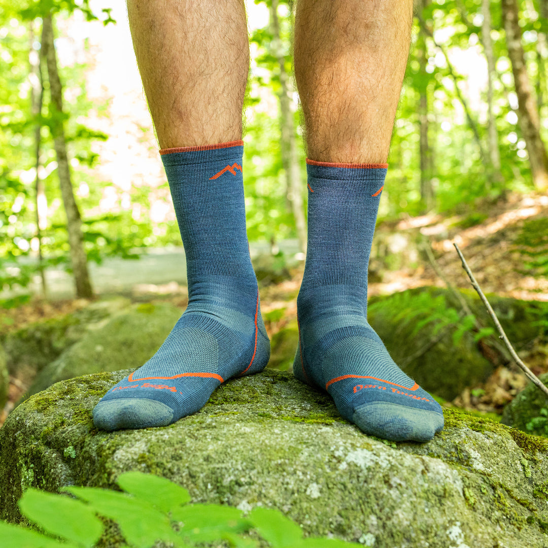 Close up shot of model standing on a rock wearing the men's light micro crew hiking sock in denim blue