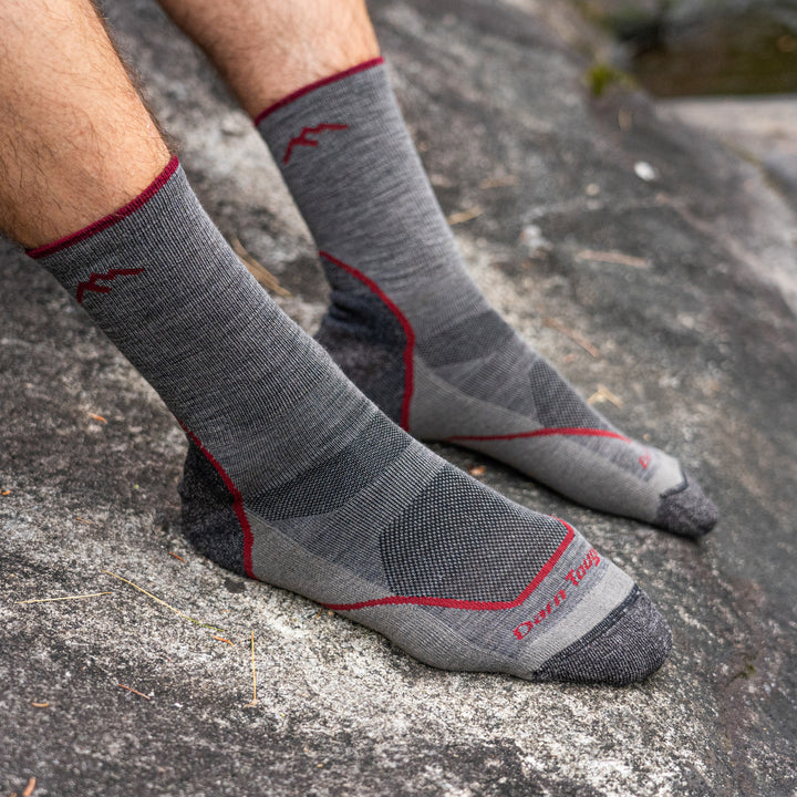 Close up shot of model sitting on a rock wearing the men's ligh micro crew hiking sock in taupe