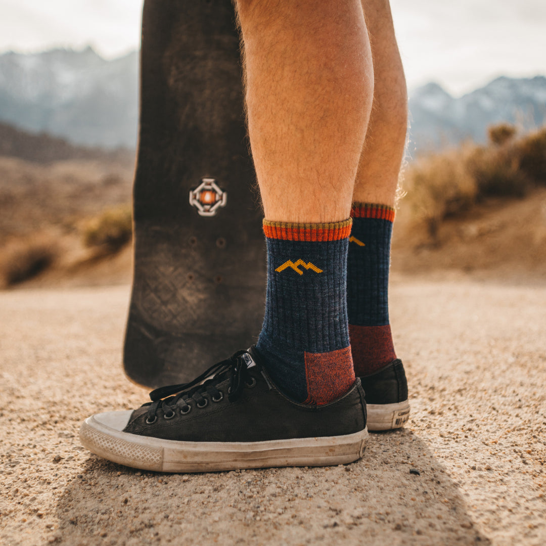 Close up shot of model standing with a skateboard wearing the mens' micro crew hiking sock in denim with black shoes