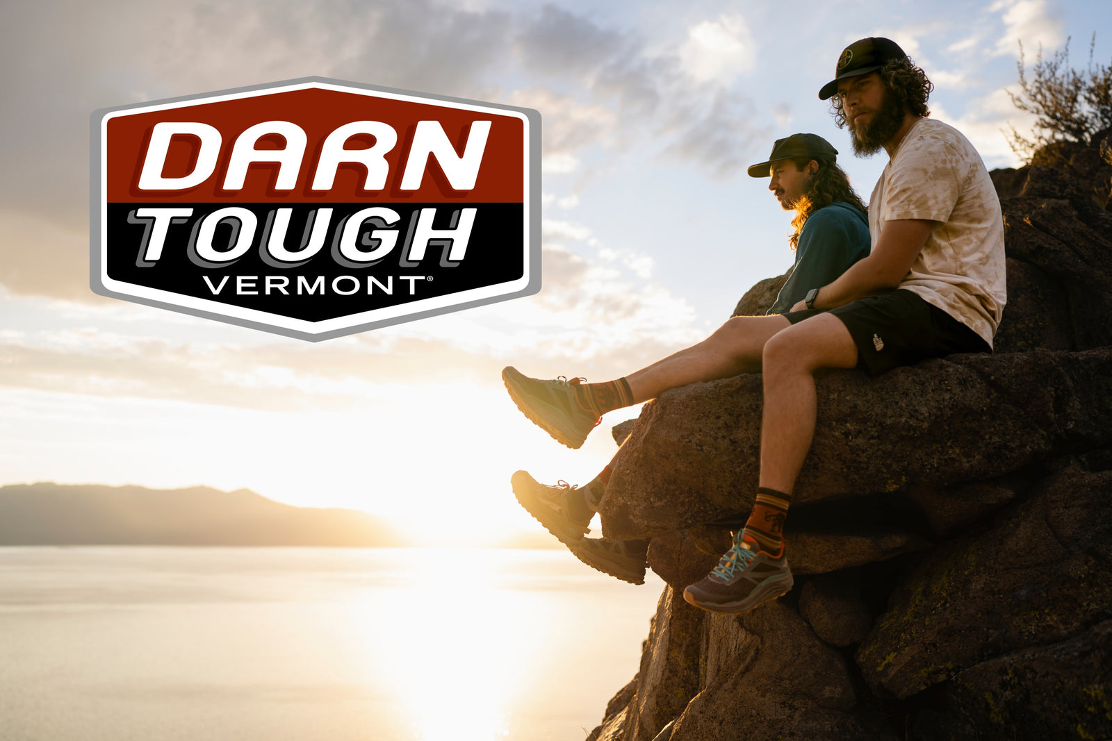 Two hikers seated on rock with Darn Tough logo overlaid