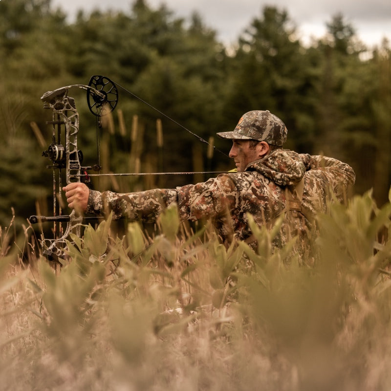 A  hunter in a field with his bow drawn, taking aim 