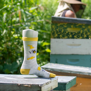 The latest Knit to Give sock with a bee and honeycomb pattern in front of an apiary