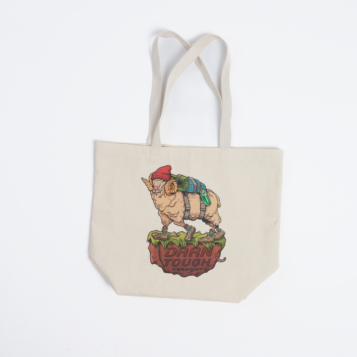 canvas tote bag with straps extended, front of bag features art work of a northern ram wearing a hat and back pack