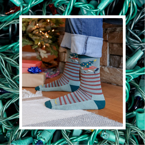 Feet wearing novelty holiday socks featuring a beaver carrying a Christmas tree