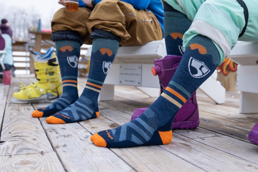 Feet wearing the High Fives ski sock, a blue sock with the foundations logo and a sunrise