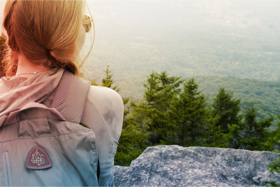A woman seated on a mountain with a 1466 day patch on her backpack