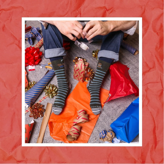 A person seated in a bunch of wrapping supplies, preparing Christmas gifts