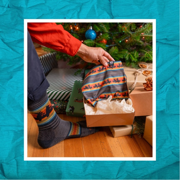 A person wearing the Willoughby sock and opening up a present that's the matching neck gaiter 