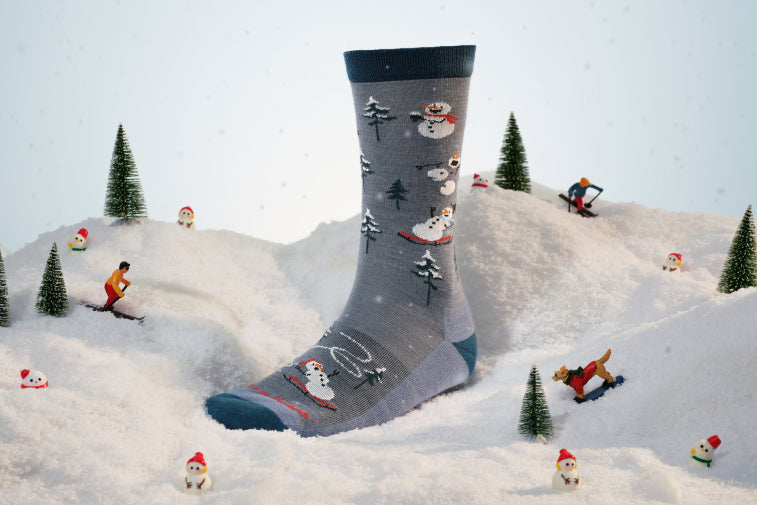 Shop Holiday Socks - A gray sock with snowmen all over it having a sledding party