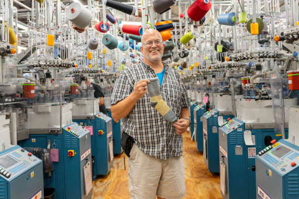 Steve laughing while he holds up the Mounainteering sock, a super cozy plush sock