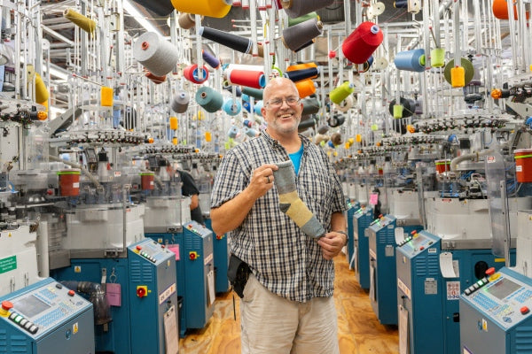 Steve laughing while he holds up the Mounainteering sock, a super cozy plush sock