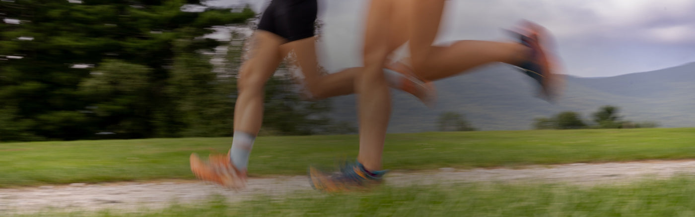Two runners going full-speed down a dirt road in Darn Tough running socks