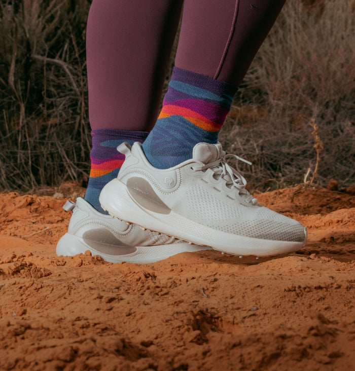A pair of feet in Micro Crew height running socks with blue mountains and a sunset patter