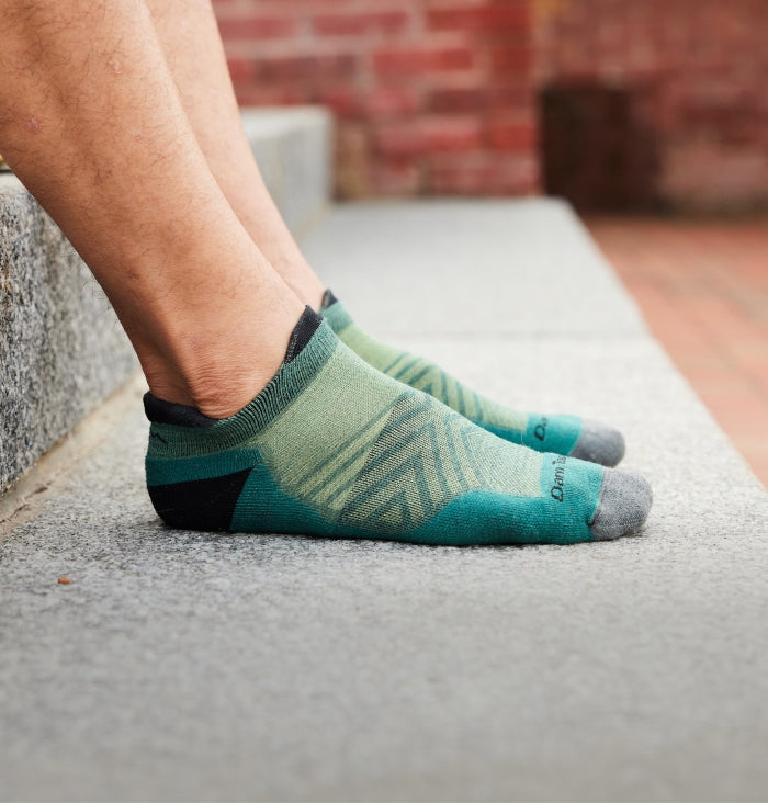 A pair of feet wearing no show tab running socks from Darn Tough in green