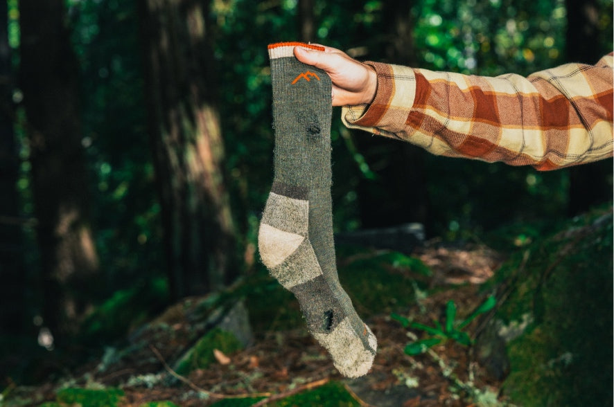 An arm holding up a threadbare, hole-y Darn Tough sock ready to be covered by our warranty