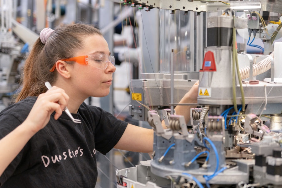 A Darn Tough employee at a knitting machine, getting ready to make an adjustment