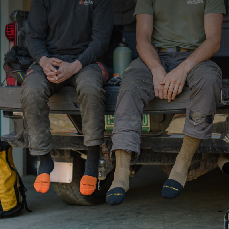 Two people seated on truck bed at a job site wearing work socks
