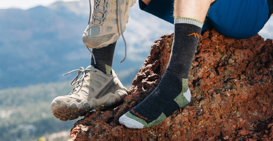 A hiker seated on the summit wearing black boot height hiking socks