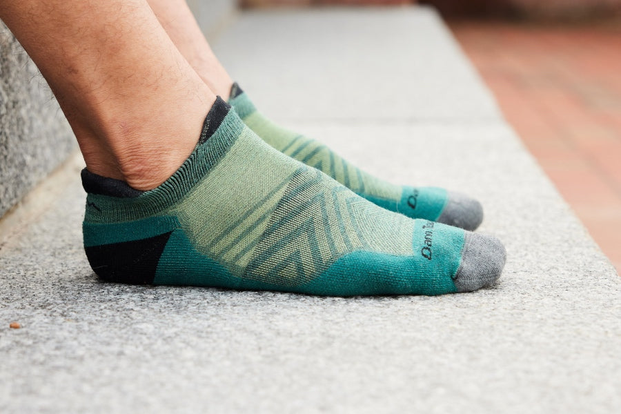 Feet wearing the men's run no show tab (no cushion) in green