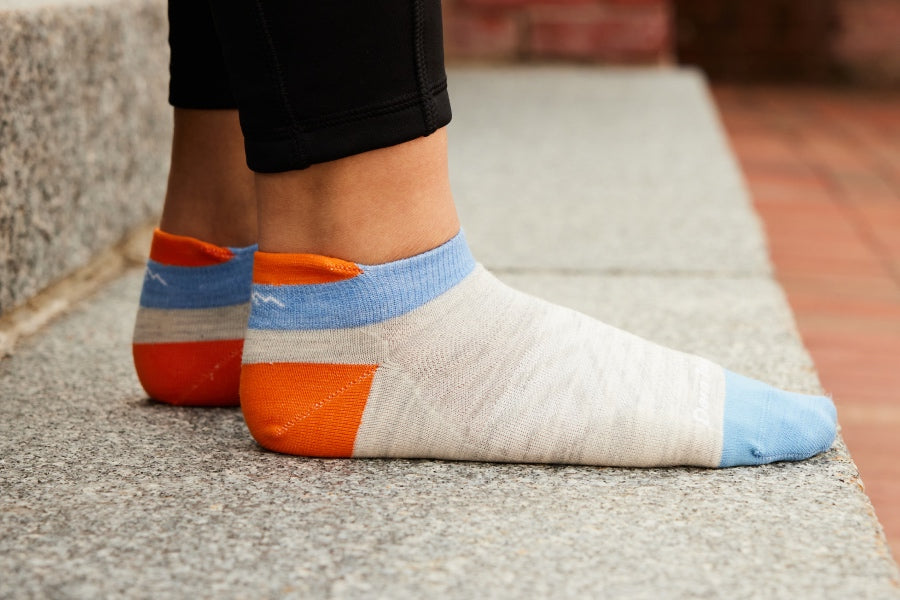 Feet wearing the women's run no show tab with cushion in ash gray with orange and blue accents