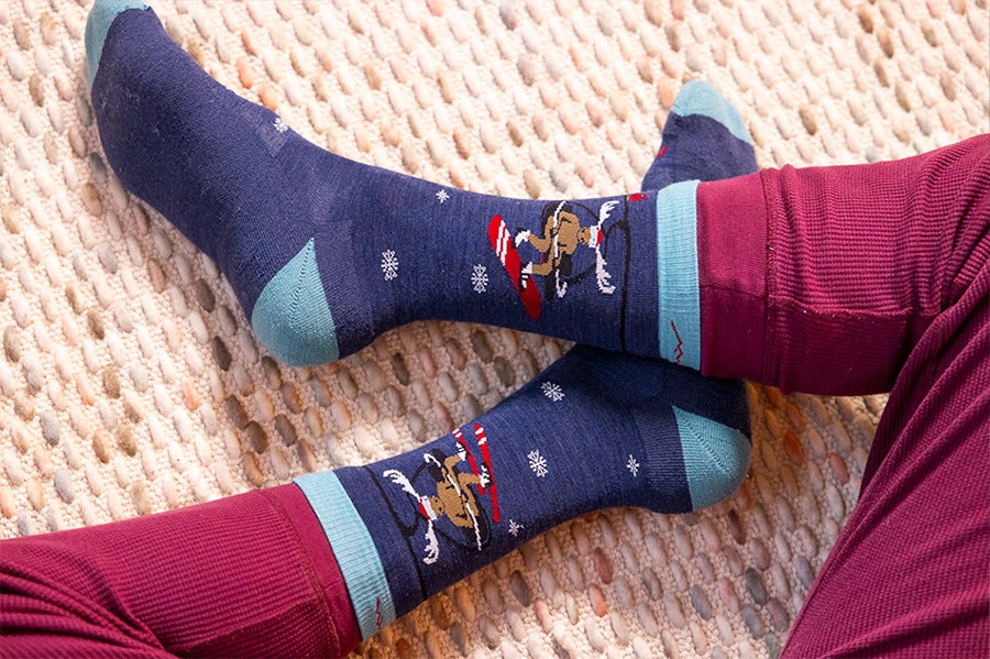 Top-down view of person sitting crosslegged wearing a sock with a snowboarding moose on a chairlift