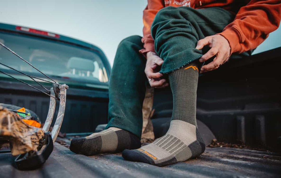 Bow hunter pulling on lightweight socks for hunting on, seated in truck bed