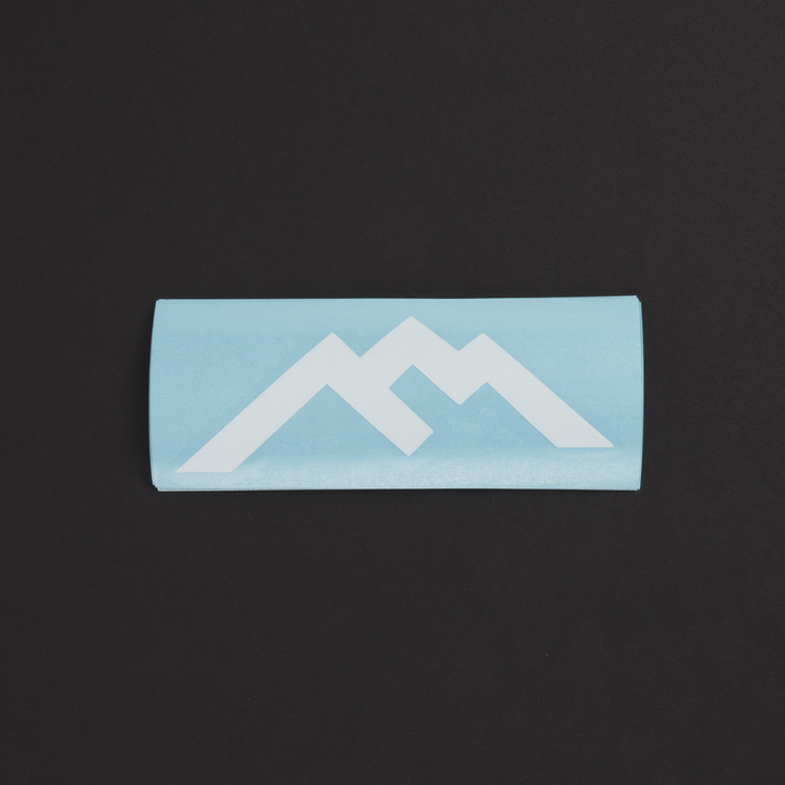 White Darn Tough mountain logo sticker with blue sticker backing against black background 