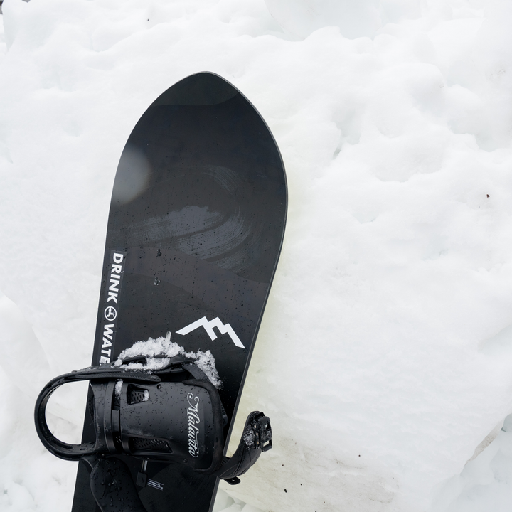 White Darn Tough mountain logo sticker on black snowboard against snowy background