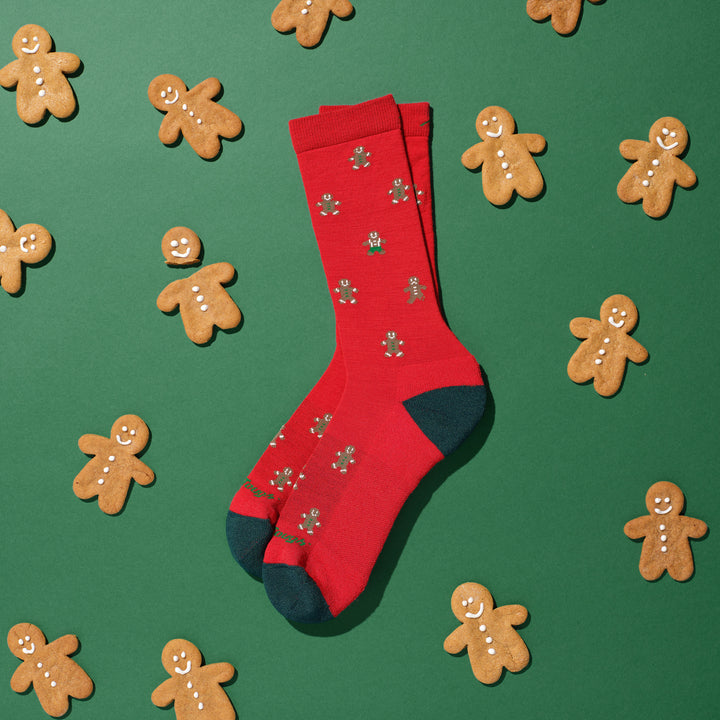 pair of gingerbread crew socks laying on green background with gingerbread cookies all around them 
