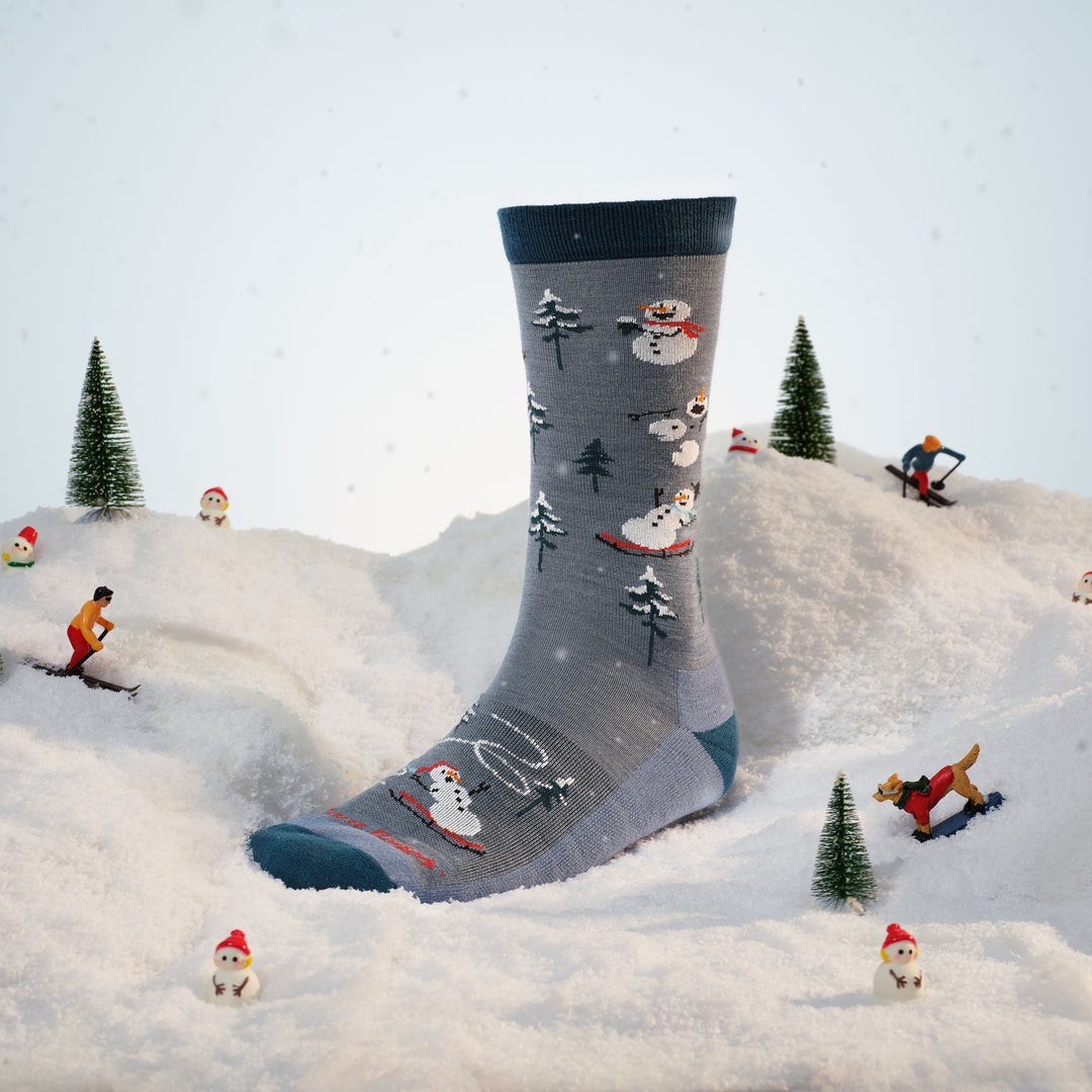 sled head crew sock on foot form placed in the snow with figures around it