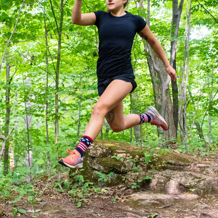 Full body mid-air jump shot of model running through the woods wearing the men's patriot micro crew running sock