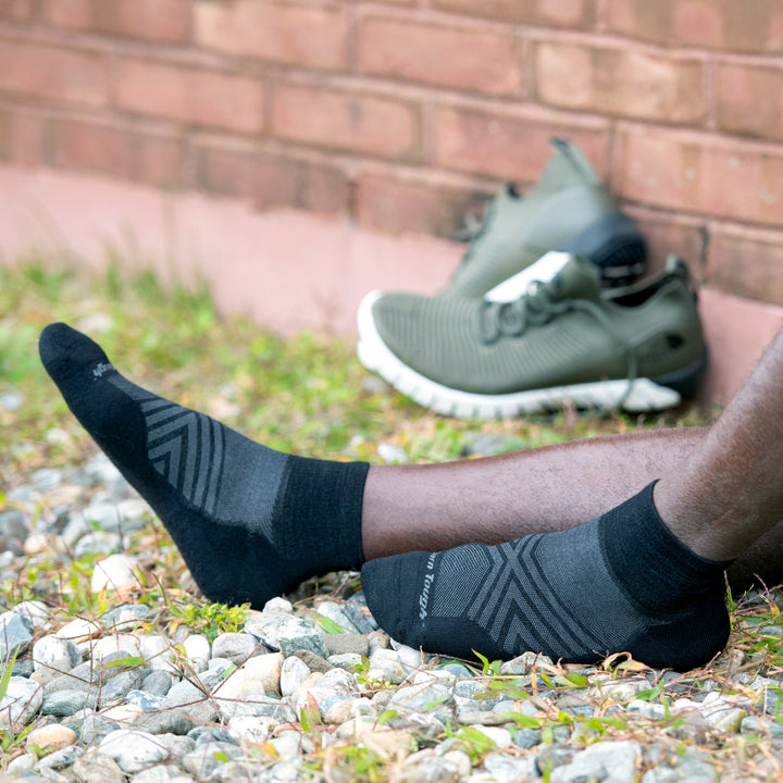 Close up shot of model sitting in the grass wearing the men's quarter running sock in black with green sneakers in the back