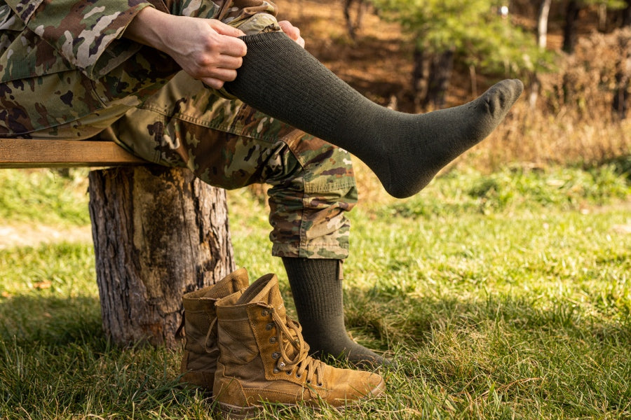 Person seated on bench pulling on socks for military boots with a performance fit