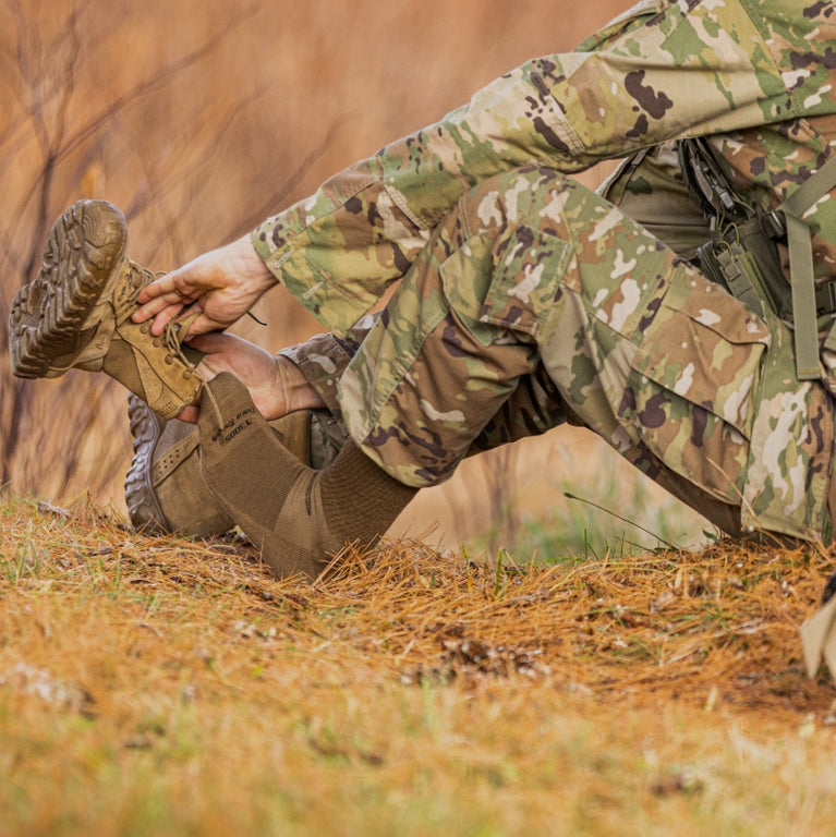 Shop Tactical Socks: Person in combat fatigues putting on boots over military boot socks