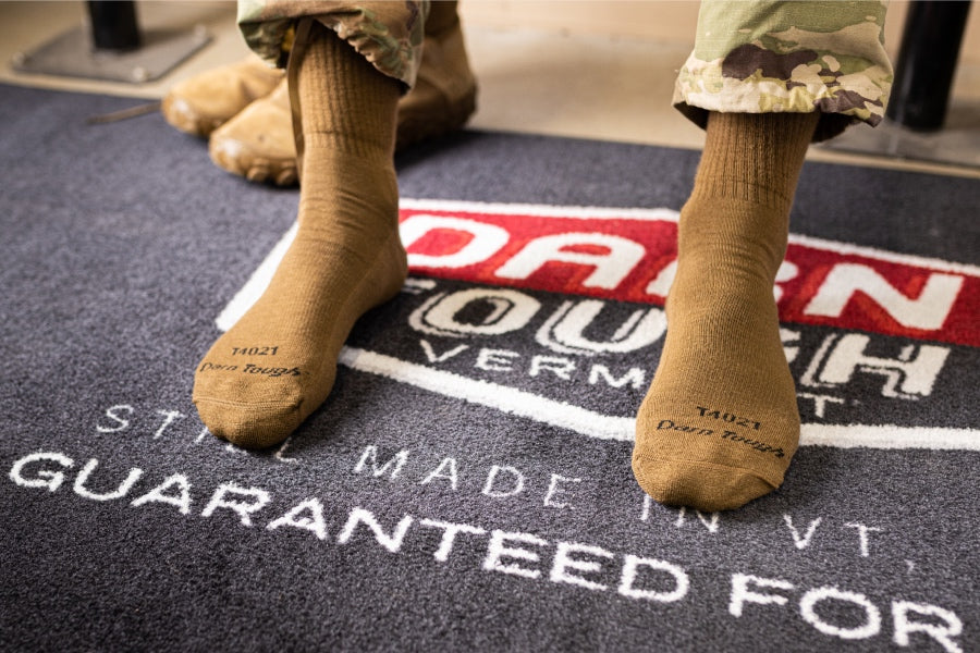 Pair of feet wearing darn tough tactical socks in ocp colors while standing on Darn Tough rug