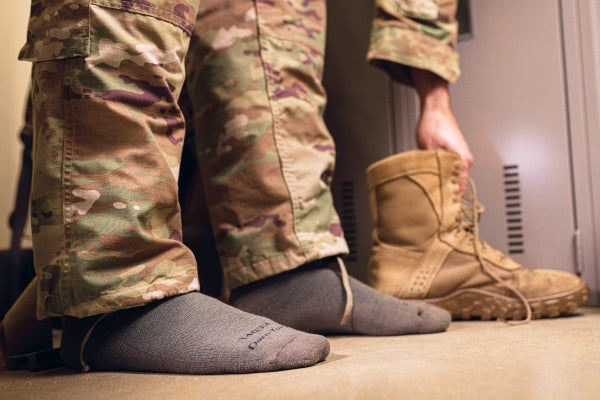 Person in camouflage putting boots down, showing their heavyweight tactical socks for extreme cold