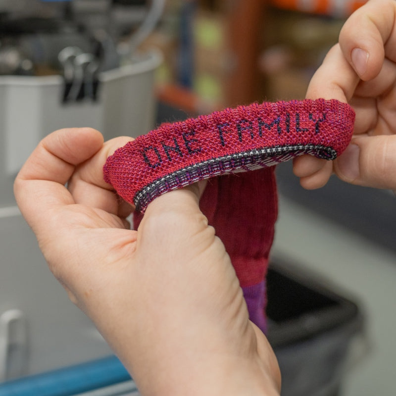 Hands showing inside of sock cuff, which says "One Family"