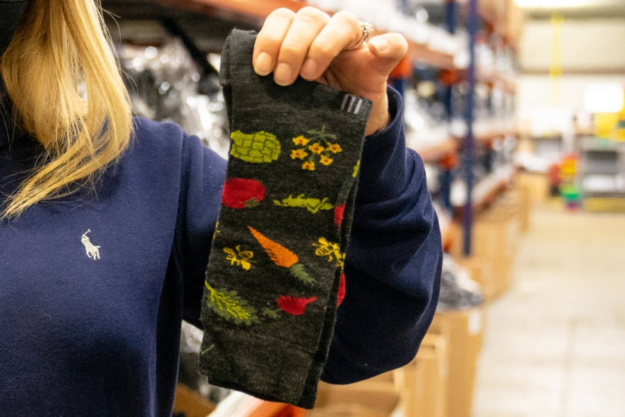 Hands holding up a sock with a vegetable design, the original Knit to Give sock