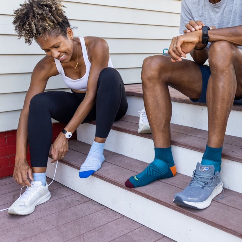 Two runners seated on steps pulling on sneakers over Run Quarter Socks from Darn Tough